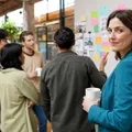 An executive pauses at the edge of her team's morning huddle, coffee in hand, watching ideas move across a sticky-note wall.