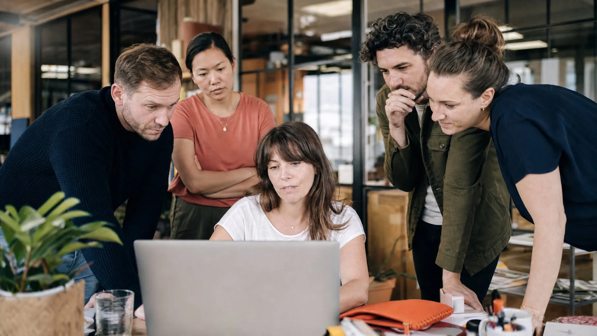 Four colleagues crowd around one desk as a teammate drives a process on her laptop.