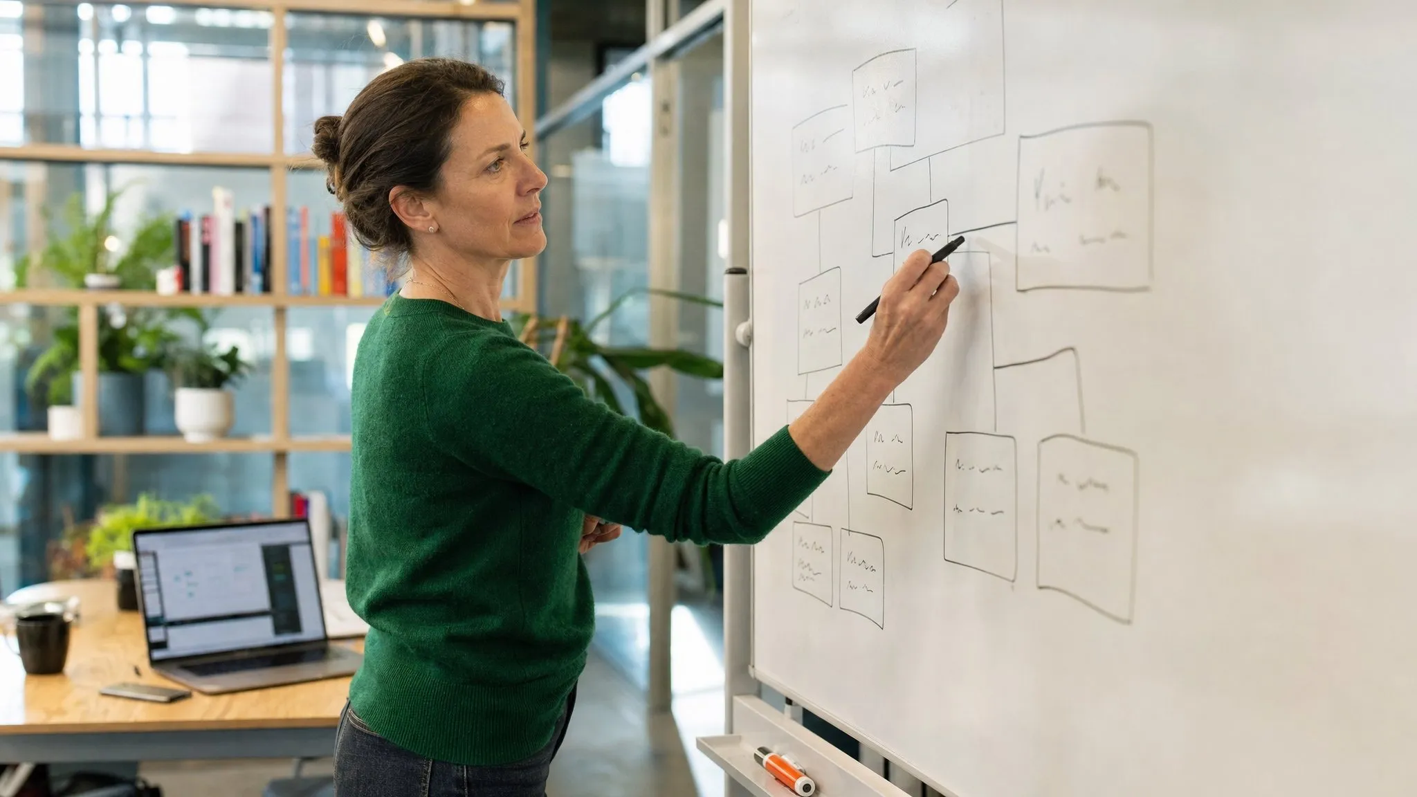 An executive sketches a workflow map of boxes and connecting lines on a whiteboard.